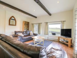 a living room with a leather couch and a tv at The Hayloft in Ripon