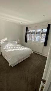 a white bedroom with a bed and two windows at Roomy 2 bed flat in London in Thornton Heath