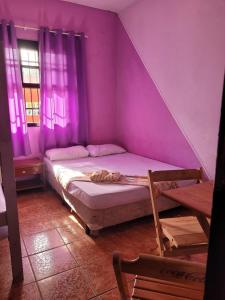 ein lila Zimmer mit einem Bett und einem Stuhl in der Unterkunft Pousada das Artes 2 in Mongaguá