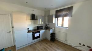 una pequeña cocina con armarios blancos y una ventana en Roomy 2 bed flat in London en Thornton Heath