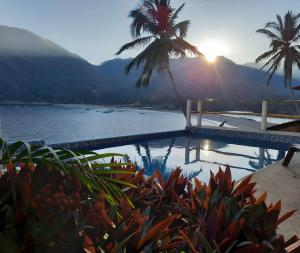 a swimming pool with palm trees and a body of water at Villa frente al mar en Yelapa para 6 personas in Yelapa