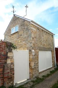 an old brick building with two white garage doors at Detached Cotswold Stone Coach House in Cheltenham