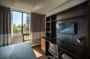 a hotel room with a bed and a desk with a television at Gage Suites at UBC in Vancouver
