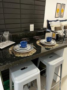 a kitchen counter with two stools with blue bowls and plates at Studio no West Fit Mossoró Alto Padrão in Mossoró