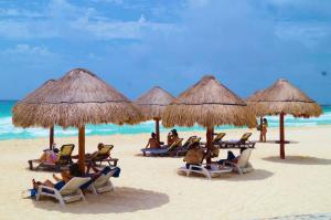 un grupo de personas sentadas en sillas bajo sombrillas en una playa en Solymar Condos, en Cancún