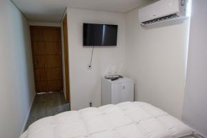 a bedroom with a white bed and a television on the wall at Suítes Container in Pomerode