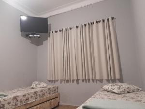 two beds in a room with curtains and a tv at Pousada Vitória in Aparecida
