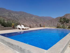 une piscine bleue avec deux chaises et des montagnes en arrière-plan dans l'établissement Dar Tamounte, à Tagadirt nʼBour