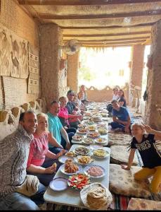 a group of people sitting around a long table of food at El Camel Hotel in Bawiti