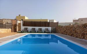 a blue swimming pool with chairs and a stone wall at Casita rural Molino de La Corte in Antigua