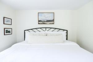 een slaapkamer met een wit bed met twee foto's aan de muur bij 1820 House - VT Charm + Modern Comforts + Hot Tub in Stowe