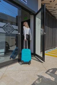 Uma mulher está a puxar uma mala azul à porta de uma loja. em Hotel StayHome em Ensenada