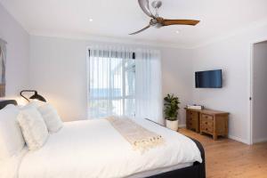 a bedroom with a white bed with a ceiling fan at O'Hara, Waterfront Merry Beach in Kioloa