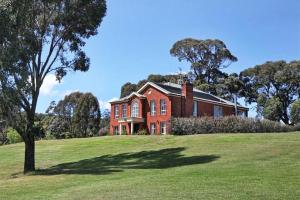 a red brick house on a grassy hill with a tree at Centelle Park Farm Stay in Kilmore East