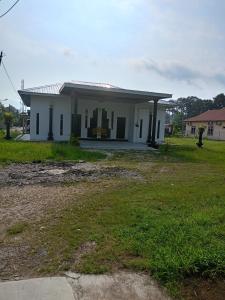 a small white house with a grass yard at Homestay ALHAQIM in Pontian Kecil