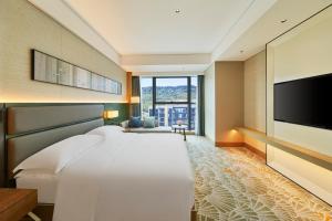 um quarto com uma grande cama branca e uma televisão de ecrã plano em Doubletree By Hilton Ya'An em Ya'an