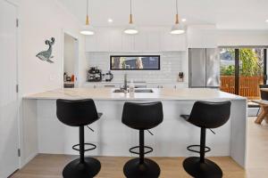 a kitchen with three bar stools in front of a counter at Leisure on Leo in Waihi Beach