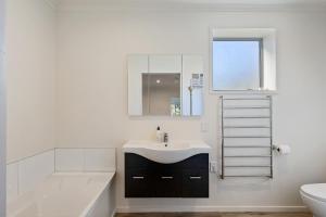 a white bathroom with a sink and a bath tub at Beachfront Favourite - Foxton Beach Holiday Home in Foxton Beach +15 photos