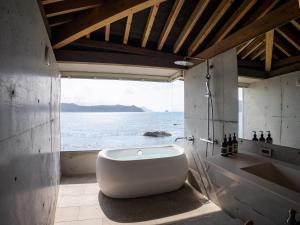 a bathroom with a tub and a view of the ocean at Denpaku The Beachfront MIJORA in Amami