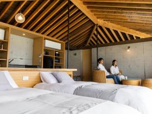 two people sitting in a room with two beds at Denpaku The Beachfront MIJORA in Amami