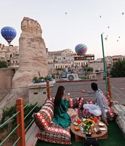 twee personen op banken op een balkon met luchtballonnen bij Vintage Cave House Hotel in Goreme