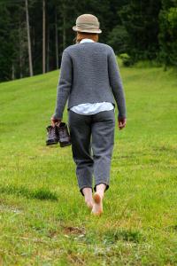 Una mujer caminando por un campo con zapatos en la mano en Posthotel Lechtal, en Holzgau