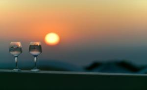 deux verres à vin assis sur une table avec un coucher de soleil en arrière-plan dans l'établissement OIA UNIQUE HOMES by K&K, à Oia