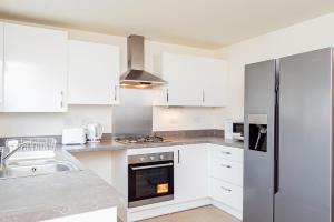 a kitchen with white cabinets and a stove top oven at Modern, Spacious House with Free Parking & Garden in Swindon