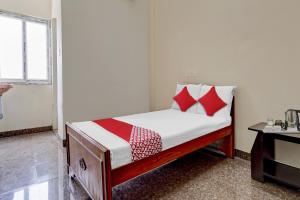 Dormitorio pequeño con cama con almohadas rojas y blancas en OYO Flagship V A S Lodge, en Punjai Puliyampatti