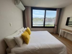 een slaapkamer met een wit bed met gele kussens en een raam bij Living in Jeju Island in Jeju-stad