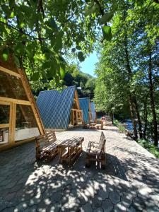 eine Terrasse mit Bänken und Tischen im Schatten der Bäume in der Unterkunft GREEN AREA in Batumi