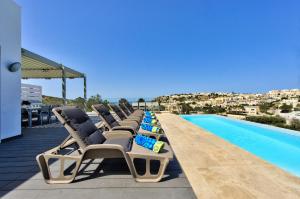 a row of lounge chairs next to a swimming pool at Villa Ghea - Indoor Jacuzzi Pool, Sauna and Games Room in Mellieħa