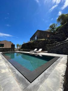 uma piscina com duas espreguiçadeiras e uma casa em Casa do Alecrim em São Roque do Pico