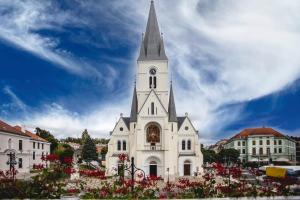 une église blanche avec un clocher et une tour d'horloge dans l'établissement Hotel Kapos, à Kaposvár