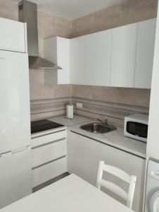 cocina con armarios blancos, fregadero y microondas en APARTAMENTOS TRES SOLES en Écija