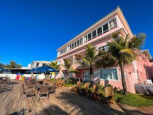 a pink building with chairs and tables and palm trees at Pousada Vila do Coral in Bombinhas