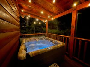 une baignoire jacuzzi installée sur une terrasse couverte éclairée dans l'établissement Elegant & Cozy Cabin Near Pigeon Forge, à Sevierville
