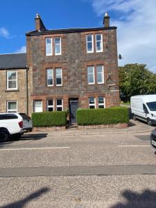 un edificio de ladrillo con coches estacionados frente a él en Roy Place Gdn Apartment, en Campbeltown