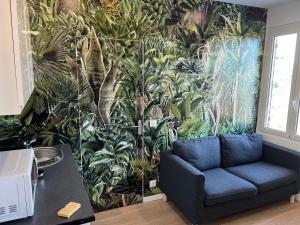 a living room with a blue couch in front of a tropical wallpaper at Appartement Nice ouest au calme 10 minutes de la plage in Nice