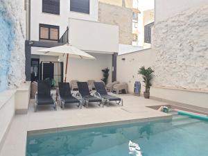 a pool with chairs and an umbrella next to a building at Bretón 17- Apartamentos con piscina climatizada en Alicante centro in Alicante