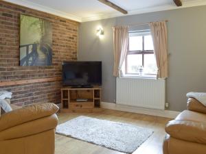a living room with a tv and a brick wall at Yr Efail Argoed in Llandowror
