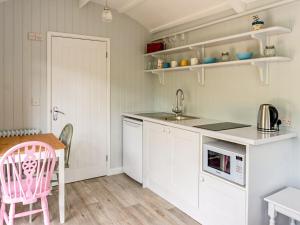 a kitchen with white cabinets and a pink chair and a table at Fig Tree Shepherds Hut in Bridport