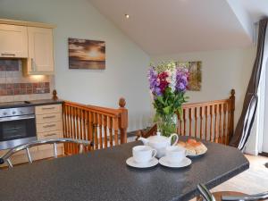 a kitchen with a table with two cups and a vase of flowers at Aprils Cottage in Kilkhampton