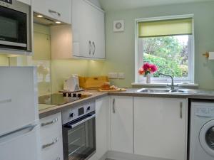 a kitchen with white cabinets and a sink and a window at Tigh Beag in Troon