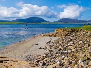 a rocky beach with a lighthouse in the water at Three Island View - W42427 in Pierowall