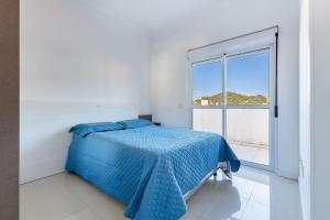 Un dormitorio blanco con una cama azul y una ventana en Cobertura Poucos Metros da Praia de Bombinhas - 2 dorms até 6 pessoas, en Bombinhas