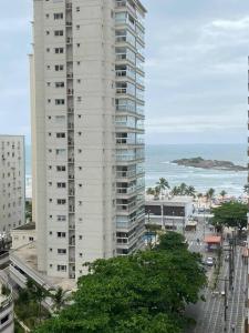 ein hohes weißes Gebäude mit dem Ozean im Hintergrund in der Unterkunft Apartamento em Pitangueiras! 70m da praia! Lindo e Aconchegante ! in Guarujá