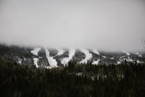 a mountain covered in snow with trees and clouds at Les Microchalets d'Édouard in LʼAnse-Saint-Jean