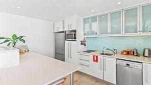 una cocina con armarios blancos y electrodomésticos de acero inoxidable en Watermark at Wategos Residence 3 Bedroom en Byron Bay
