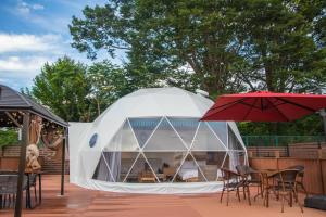 uma tenda cúpula branca com cadeiras e um guarda-sol vermelho em Gramercy Village 山中湖 Glamping &Sauna em Yamanakako